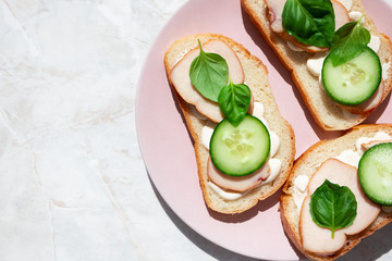 Sandwiches with ham, basil leaves and cucumber on pink plate on marble table with copy space. Details of food
