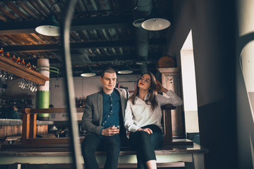 Cheerful caucasian man and woman talking, enjoying at the alco shop, cafe, bar. Couple or friends, having a date, romantic. Wearing casual attire. Emotional, smiling. Communication, relations concept.