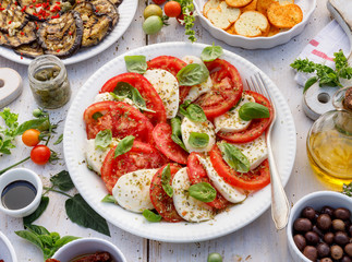 Traditional italian food, Caprese salad made of sliced fresh tomatoes, mozzarella cheese and basil  served on a white plate on a wooden table, top view