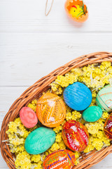 Multi-colored Easter eggs in a basket on a white wooden background