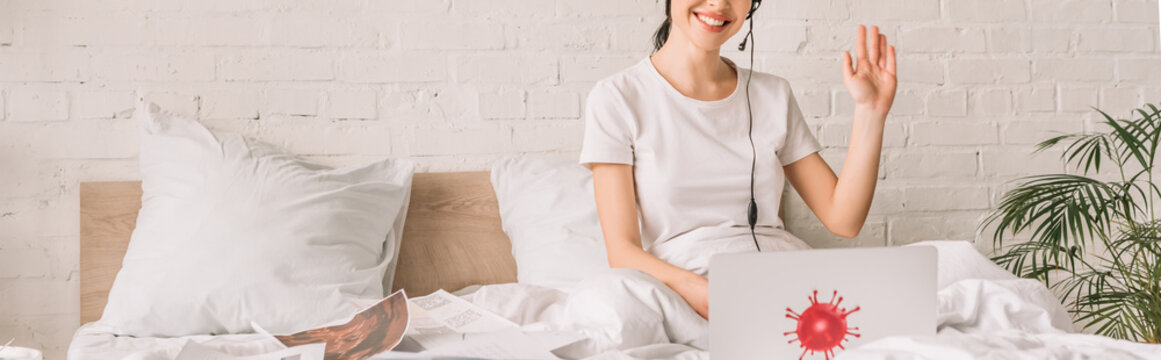 Cropped View Of Remote Operator In Headset Waving Hand While Working In Bed Near Laptop With Coronavirus Bacteria Sticker, Panoramic Orientation