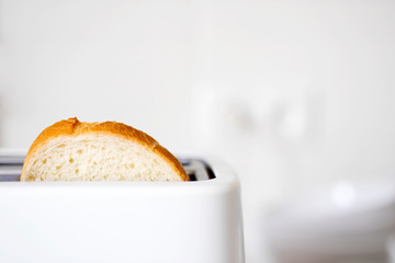 A piece of bread in a toaster on the background of a white ceramic blurred kitchen wall - obrazy, fototapety, plakaty