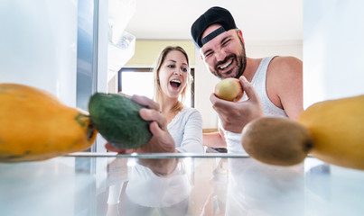Young couple open the fridge at home while choosing organic fruits during quarantine isolation -...