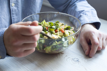 A man in a blue office shirt is sitting at a table with a bowl of salad. Cherry tomato salad with rucola, radicchio, lettuce, feta cheese, olive oil and balsamic dressing