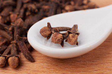 A spice of dried cloves lies on a wooden spoon and is scattered on old wooden boards near the bag. Spices cloves for cooking. Close-up.