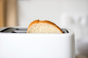 A piece of bread in a toaster on the background of a white ceramic blurred kitchen wall - obrazy, fototapety, plakaty