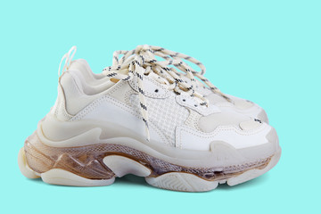 Pair of new trendy beige sneakers isolated on a light blue background with shadow. Side view.