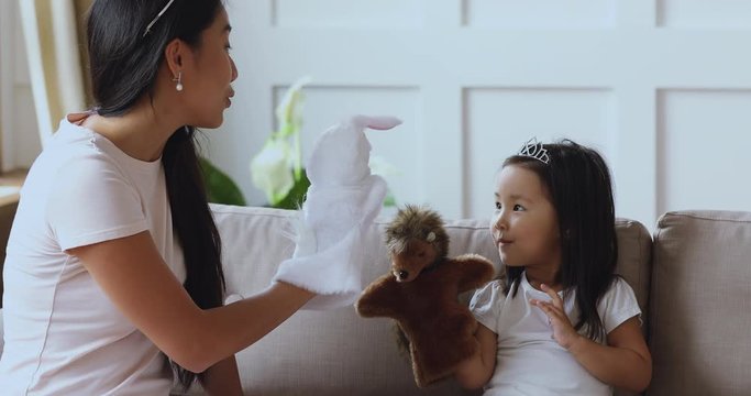 Pretty millennial elderly asian ethnicity sister playing puppet hand toys with cute little preschool girl. Happy young vietnamese mother having fun with small kid daughter, enjoying weekend playtime.