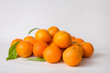 Whole orange fruits heap with green leaves isolated on white background. Closeup shot. Natural vitamin or organic food concept