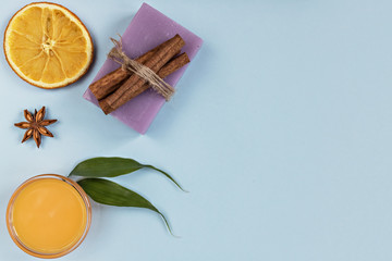 On a blue background are care products: lavender soap and mango cream for face and body after, coffee scrub. For aromatherapy: cinnamon sticks, anise star, sliced orange circles. Spa home concept.