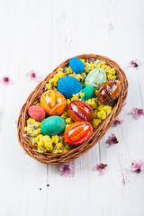 Multi-colored Easter eggs in a basket on a white wooden background