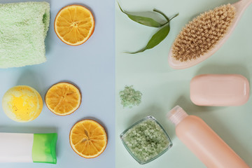 On a blue-green background are care products: shower gel, soap, sea salt and scrub, brush body, bath bomb, body milk after a bath, towel,sliced oranges in circles. The concept of home spa