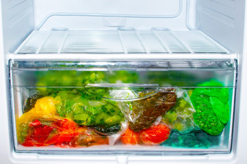 A colorful variety of frozen vegetables in a freezer container. Storage of different vegetables in packages in the box of the refrigerator.