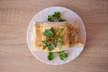 Pita with greens on a white plate on the wooden table, delicious Breakfast made at home. Traditional Middle Easter fast food. Homemade dish. 