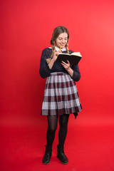 schoolgirl teen with two pigtails in a jumper and checkered skirt with a book in hand on a red background