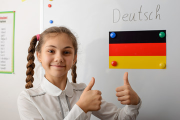 Happy learner showing thumbs up near flag of Germany on the blackboard. Learning foreign languages,...