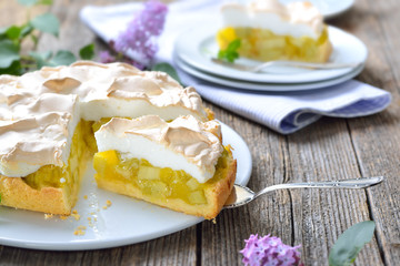 Leckerer Rhabarberkuchen mit Baiserhaube auf einem Holztisch mit frühlingshafter Fliederdeko - ...