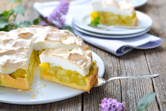 Leckerer Rhabarberkuchen mit Baiserhaube auf einem Holztisch mit frühlingshafter Fliederdeko -  Delicious rhubarb cake with springlike lilac decoration