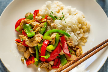 Spicy asian chicken pieces with red and green peppers with rice on plate.