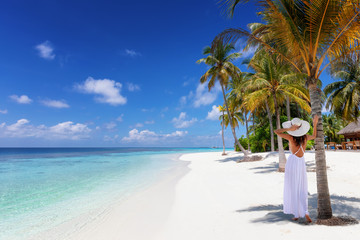 Tropisches Reisebanner mit einer Frau mit weißem Hut die an einem tropischen Traumstrand mit Palmen und türkisem Meer steht und die Aussicht genießt, Malediven