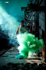 Fototapeta premium a man with a sports figure in the factory confidently passes through green smoke.