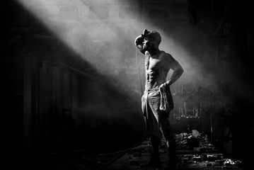 Obraz premium strong man against fog at factory exhausted stands, press and lateral abdominal muscles and pectoral muscles illuminated by light, place for text.