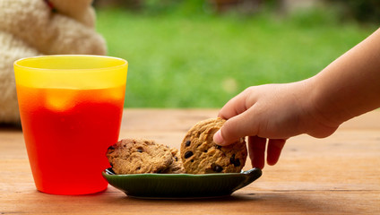 Girl hand pick up cookie from a green plate near glass of strawbarry juice on wooden table. Enjoy stay at home with warmth family.