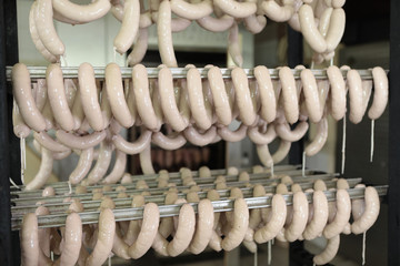 A worker at the meat processing factory, prepares sausages at the work table. Food processing and processing industry. Raw meat mix: steaks, poultry, sausages, ham, chopped, minced meat. 