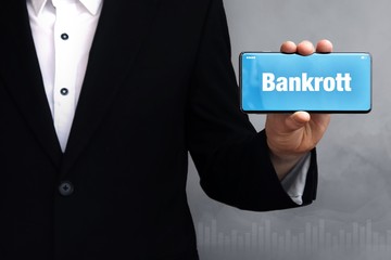 Bankrott. Geschäftsmann im Anzug hält ein Smartphone in die Kamera. Der Begriff Bankrott steht...