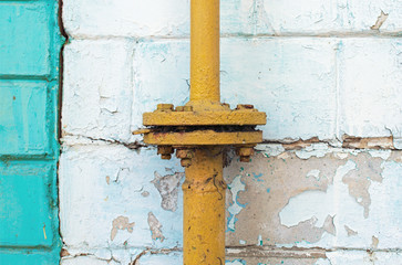An old yellow gas pipe with flange connection. A white brick on peeling wall. Abstract background