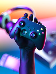 Hand Holding Wireless Joystick With Gaming Gamepad Controller, VR Goggles, Headphones, Video Game Console On Background. 3d rendering © ekostsov