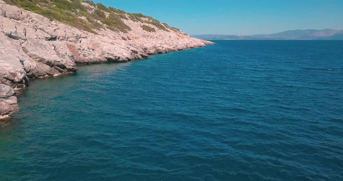 Slow forward and crane down drone shot next to a rocky shore in the aegean sea, Greece. 4K video quality