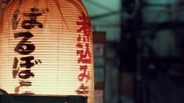 Close-up Chinese or Japanese letters orange lanterns swaying in slow motion. Night lifestyle. Decoration paper lantern with warm orange and yellow light