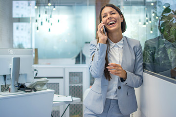 Happy young businesswoman in formal-wear talking on mobile phone in office