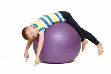 The child is engaged with a large gymnastic ball. Fitness exercises at home during a pandemic. Boy on the ball Isolated on a white background.