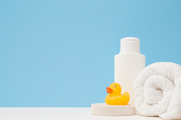 White shampoo bottle, towel and wisp. Yellow rubber duck. Body washing concept. Close up. Front view. Empty place for text or logo on light blue background. Pastel color.