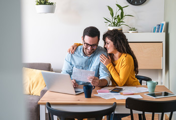 Positive young couple embracing and paying household bills or taxes on laptop online at home stock photo - obrazy, fototapety, plakaty