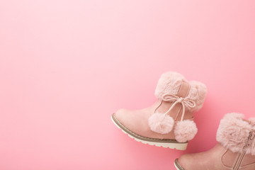 Leather warm baby boots with fluffy balls on light pink table background. Pastel color. Empty place for text. Closeup. Top down view.