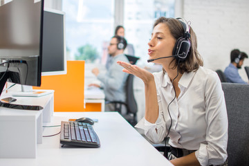 Attractive young operator woman blowing a kiss to computer screen during video call.