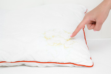 Young woman hand finger pointing to saliva stain on white pillow. Cleaning problem and solution...