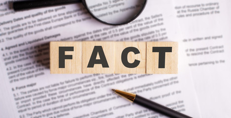 Obraz premium fact word made up of wooden cubes on the background of a contract with pen