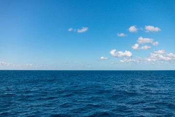 Obraz premium A blue sea under a blue sky with white clouds hovering over it