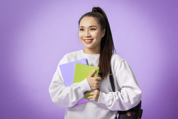 Portrait of beautiful young asian holding notebooks isolated on the violet background
