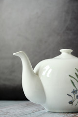 Detail of classic ceramic teapot on wooden table with dark background. Copy space