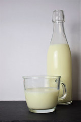 
Glass cup with milk, close-up, behind the bottle