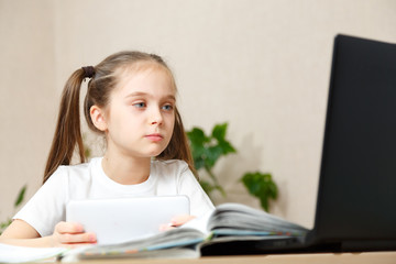 Fototapeta na wymiar Little girl doing her homework at home and using a laptop