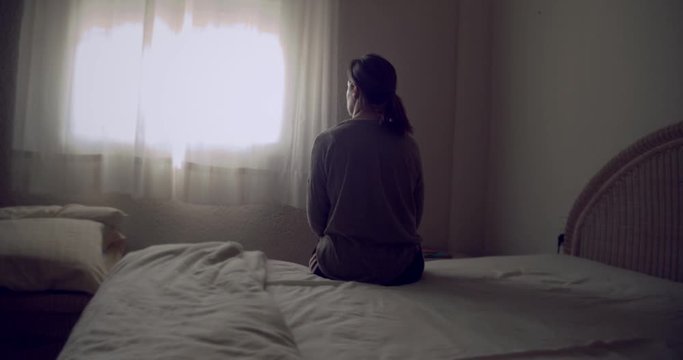 Mujer melanc&oacute;lica sentada en la cama mirando por la ventana