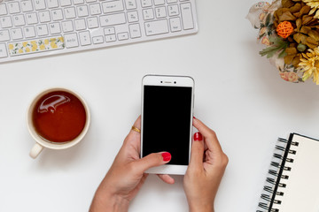 Home office telecommuting desk with girl hands on phone. Top view, flat lay perspective