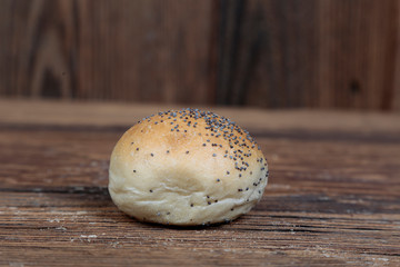 View of a handmade, fresh, round bread roll sprinkled with poppy seeds on a wooden, brown, rustic table.