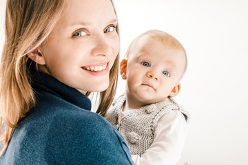 Beautiful mother and child smiling at camera. Portrait of happy young mother holding adorable infant baby girl isolated on white background. Parenthood concept